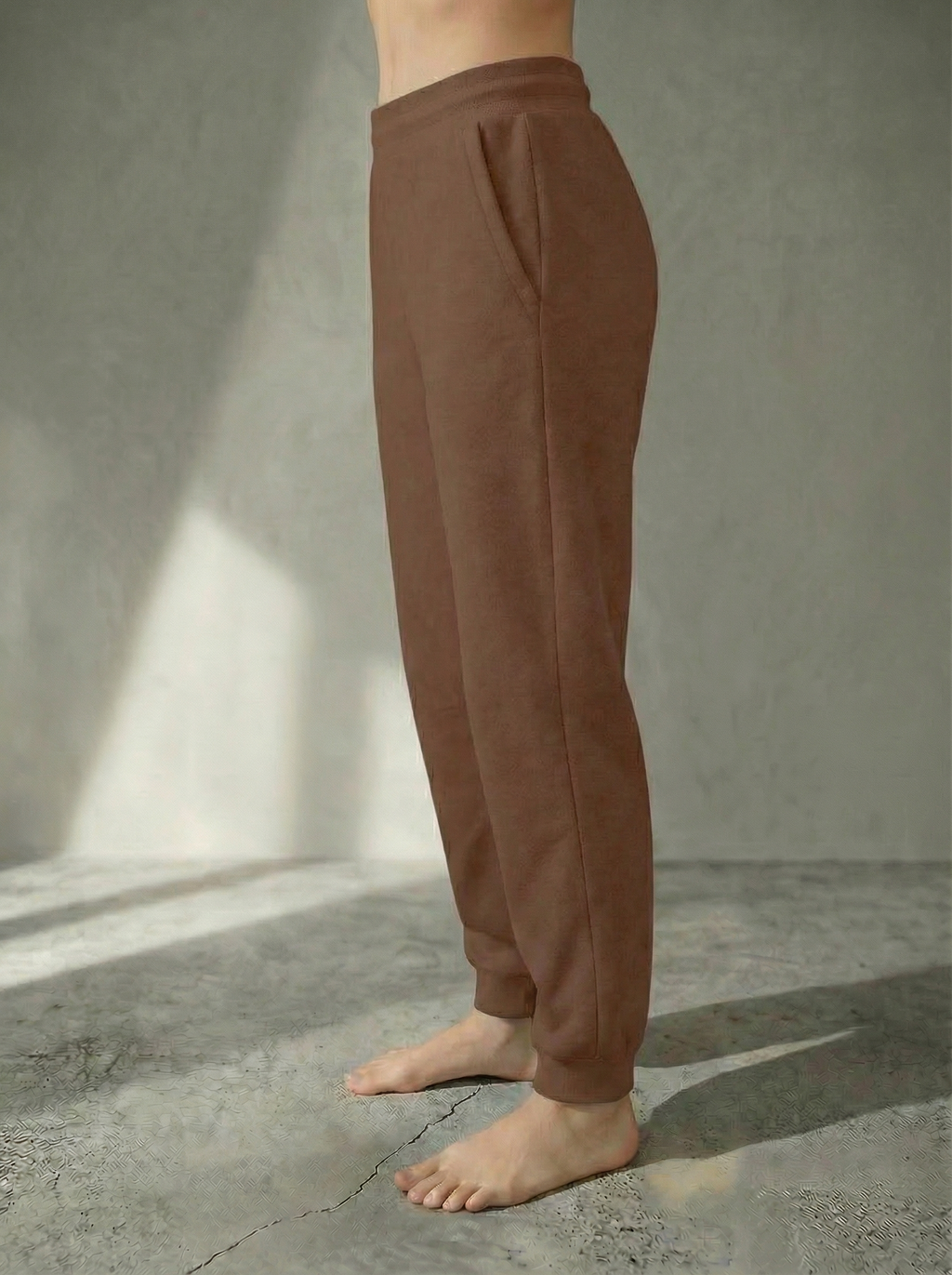 Side view of the Deryn Jogger women’s luxury jogger pants by BOU Clothing in Tan, shown on a model standing barefoot against a beige backdrop.