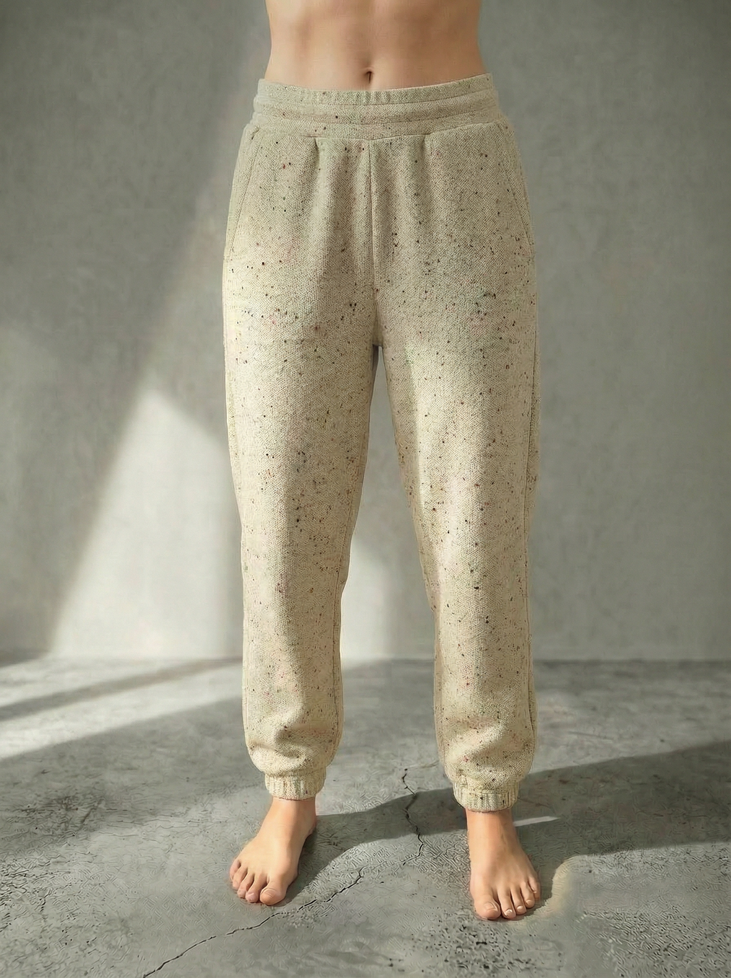 Front view of the Deryn women’s luxury jogger pants beige with red fleck  colour, by BOU Clothing shown on a model standing barefoot against a stone grey  backdrop.