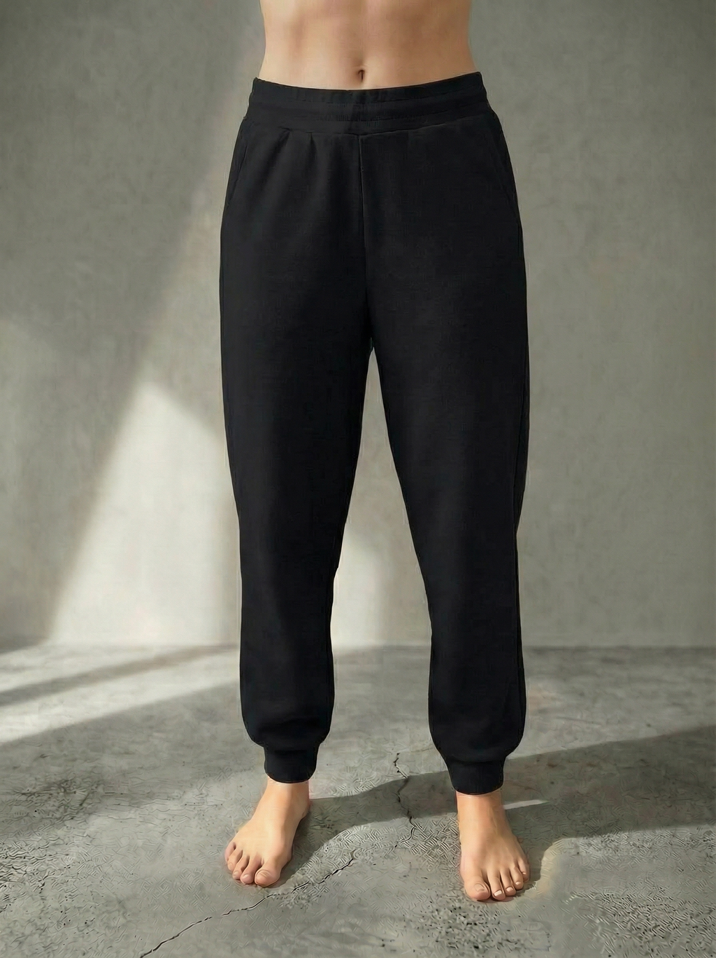 Front iew of the Deryn women’s luxury jogger pants Black colour, by BOU Clothing shown on a model standing barefoot against a stone grey  backdrop.