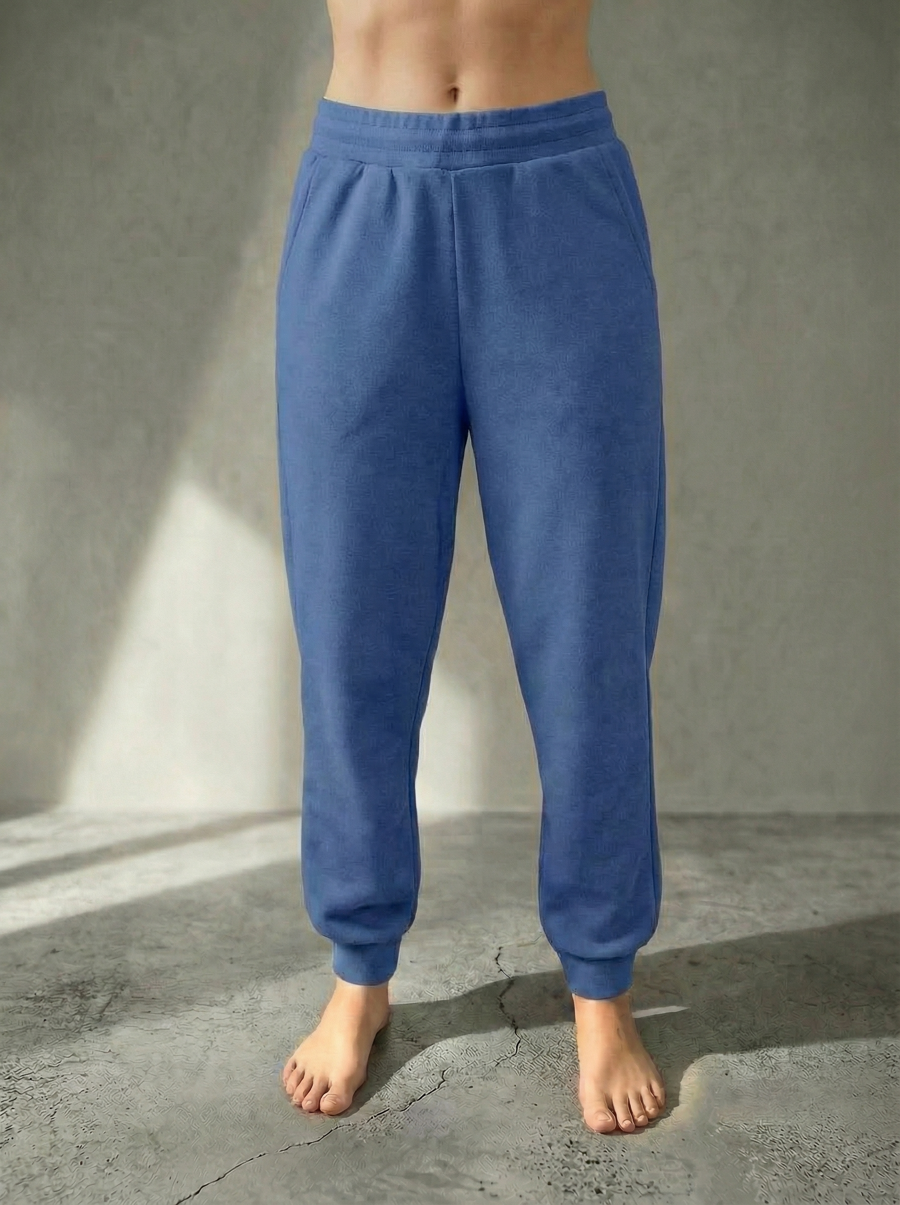 Front view of the Deryn Jogger women’s luxury jogger pants in Denim, by BOU Clothing shown on a model standing barefoot against a stone grey  backdrop.