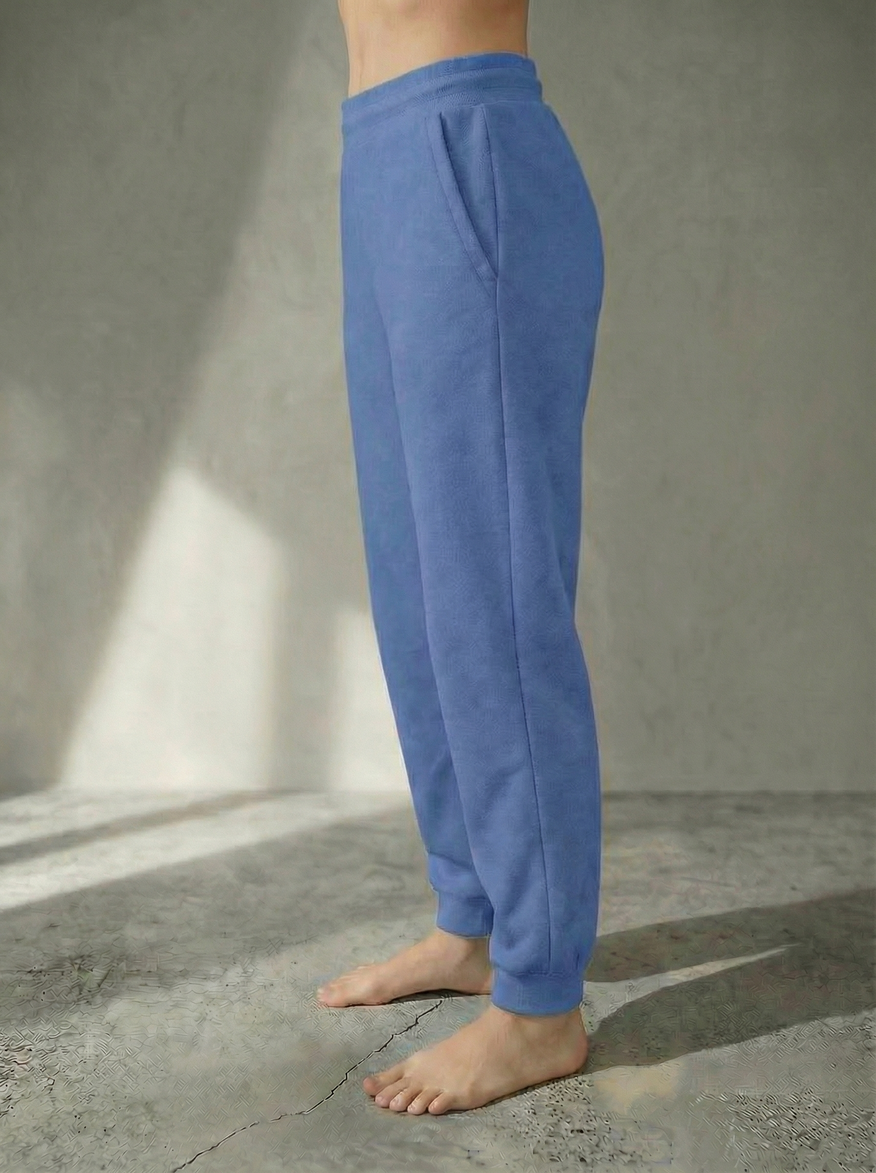Side view of the Deryn Jogger women’s luxury jogger pants in Denim, by BOU Clothing shown on a model standing barefoot against a stone grey  backdrop.