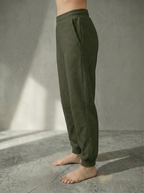 Side view of the Deryn Jogger women’s luxury jogger pants in Forrest colour by Bou Clothing, shown on a model standing barefoot against a stone grey backdrop.